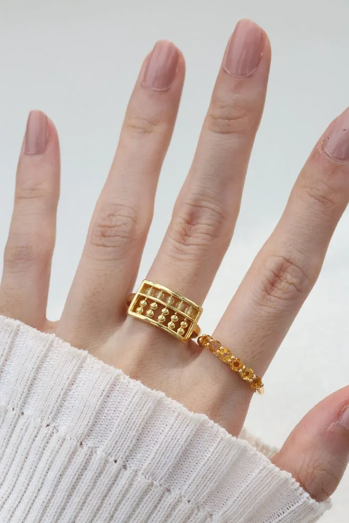A model wearing the yellow gold abacus ring featuring a rectangular frame with golden beads and yellow citrine stones, designed to mimic a traditional abacus, adding a playful and unique touch to your jewelry collection.