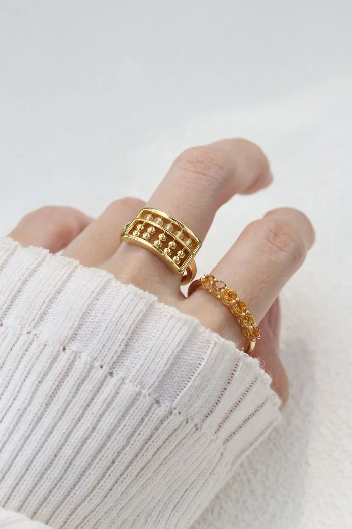 A model wearing the yellow gold abacus ring featuring a rectangular frame with golden beads and yellow citrine stones, designed to mimic a traditional abacus, adding a playful and unique touch to your jewelry collection.