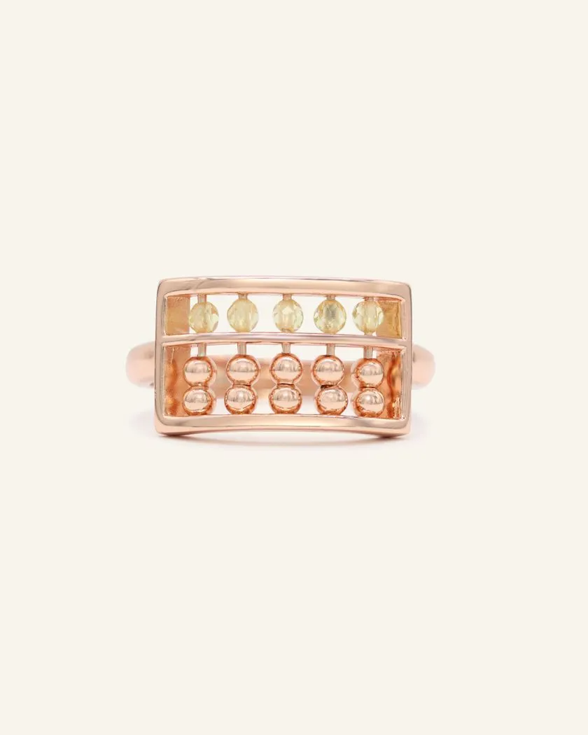 A rose gold abacus ring featuring a rectangular frame with golden beads and yellow citrine stones, designed to mimic a traditional abacus, adding a playful and unique touch to your jewelry collection.