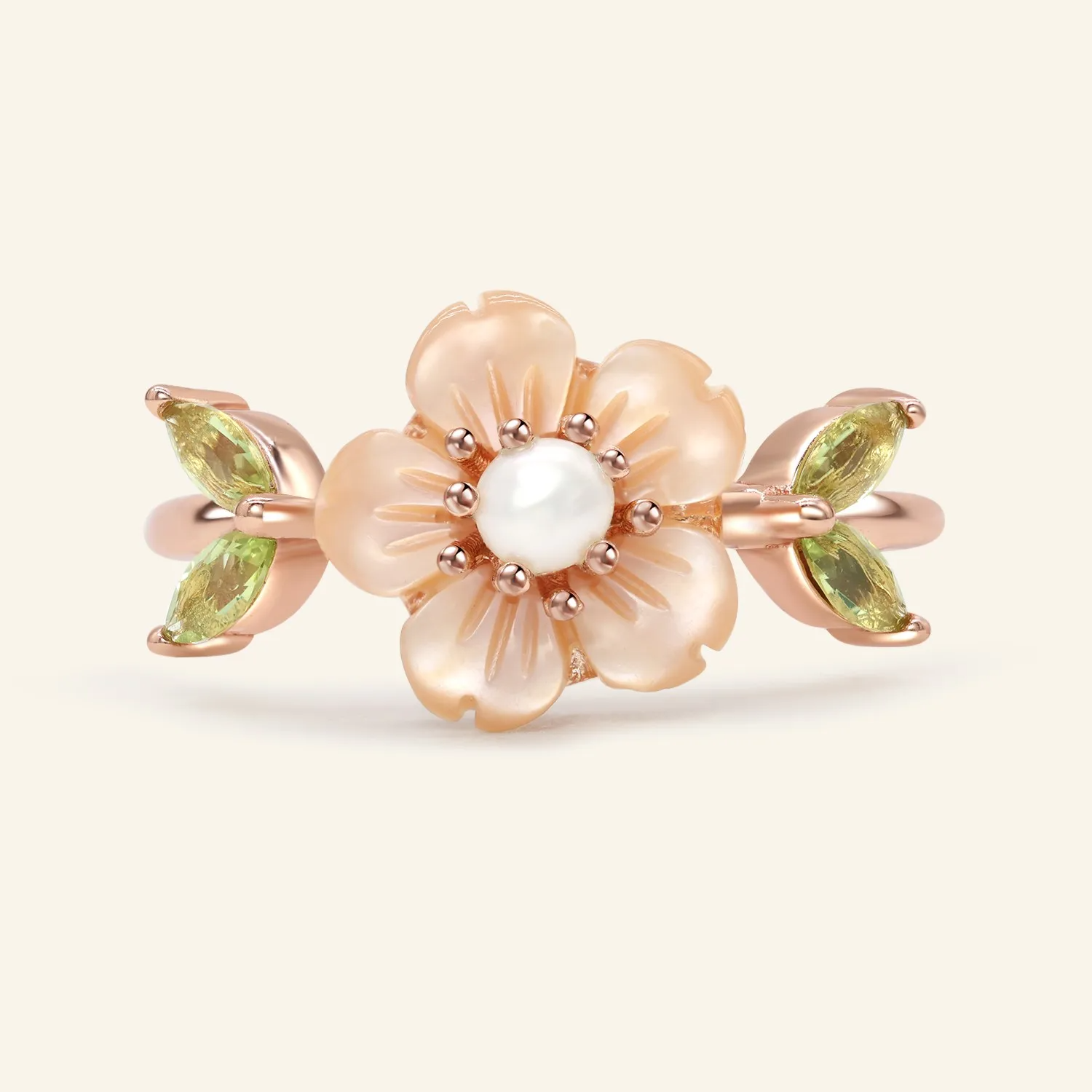 A delicate sakura blossom ring in rose gold featuring a central freshwater pearl, surrounded by hand-carved shell petals resembling cherry blossoms, with peridot stones set as the leaves on either side.