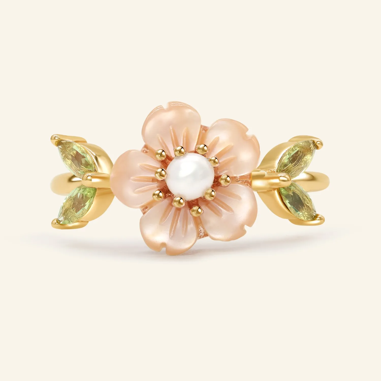 A delicate sakura blossom ring in yellow gold featuring a central freshwater pearl, surrounded by hand-carved shell petals resembling cherry blossoms, with peridot stones set as the leaves on either side.