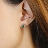 A model wearing a pair of elegant earrings, each featuring a one carat green moissanite stone set in a bezel rose gold setting.