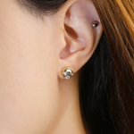 A model wearing the Modern and minimalistic one-carat gunmetal grey moissanite bezel studs set in yellow gold, exuding understated elegance with a sleek metallic sparkle.