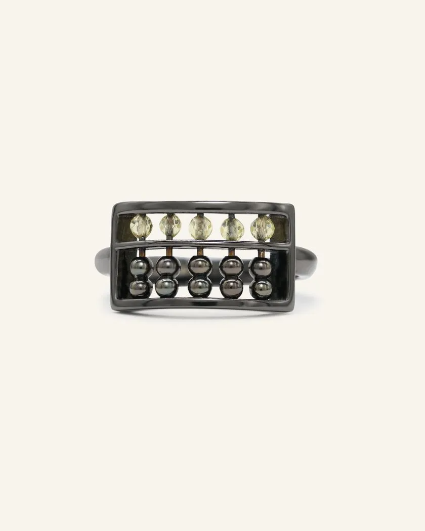 A black gold abacus ring featuring a rectangular frame with golden beads and yellow citrine stones, designed to mimic a traditional abacus, adding a playful and unique touch to your jewelry collection.