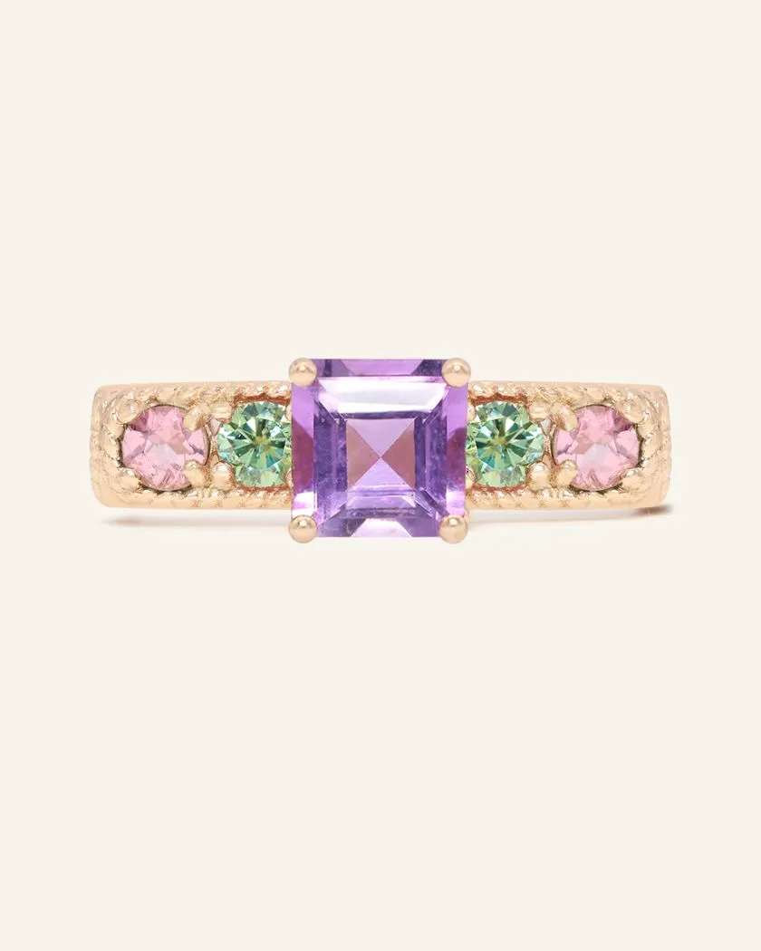 A rose gold ring featuring a central square-cut amethyst stone, flanked by two pink tourmalines and two green moissanites on either side, set in a textured band,