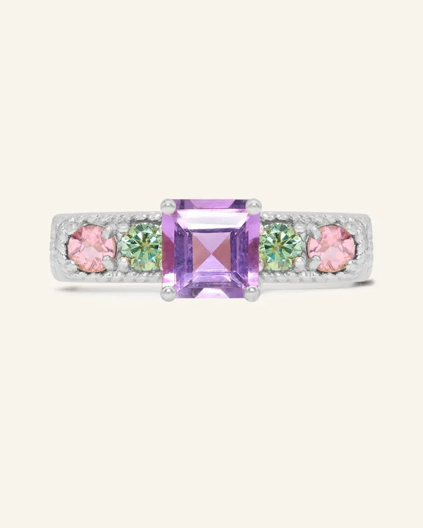 A silver ring featuring a central square-cut amethyst stone, flanked by two pink tourmalines and two green moissanites on either side, set in a textured band,