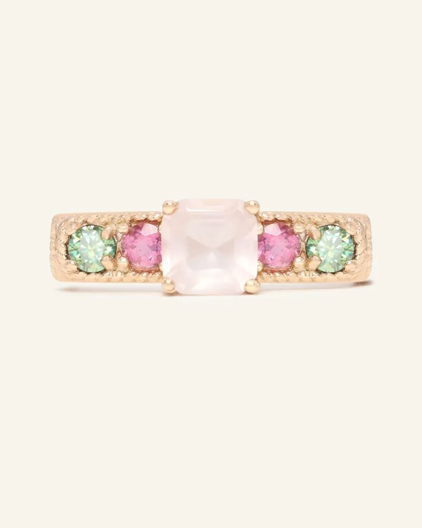 A rose gold ring featuring a central square-cut rose quartz stone, flanked by two pink tourmaline and two green moissanites on either side, set in a textured band.