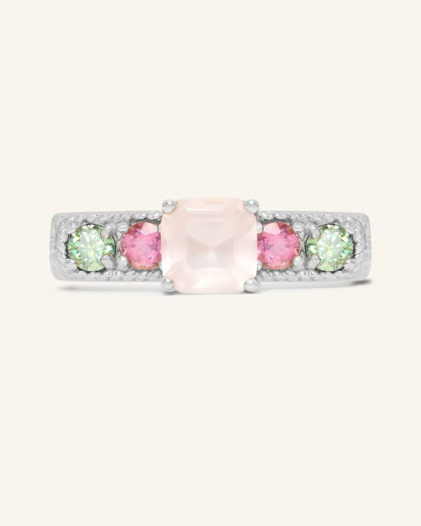 A silver ring featuring a central square-cut rose quartz stone, flanked by two pink tourmaline and two green moissanites on either side, set in a textured band.