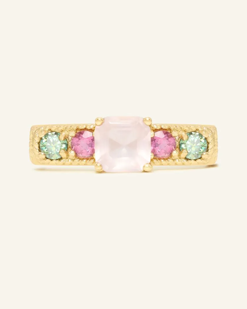 A yellow goldring featuring a central square-cut rose quartz stone, flanked by two pink tourmaline and two green moissanites on either side, set in a textured band.