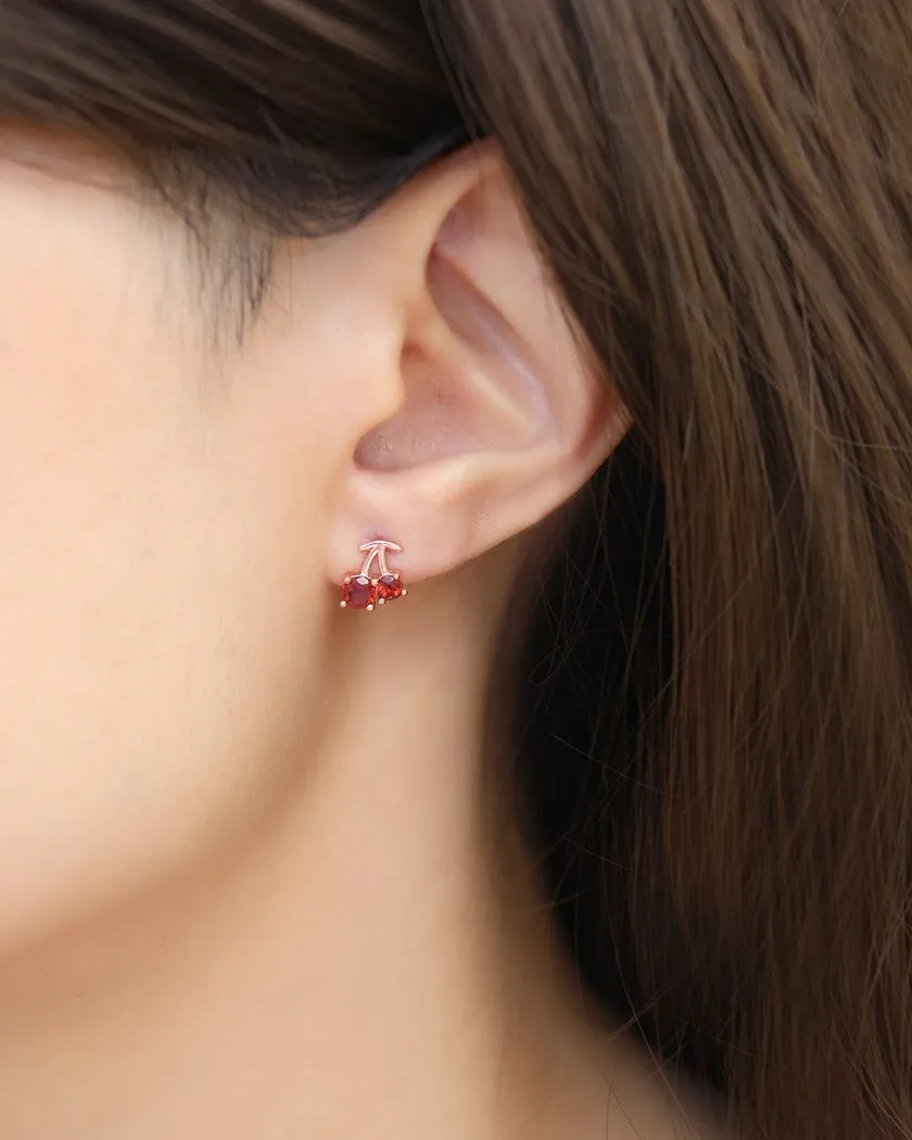 Cherry Garnet Studs worn by a model. Delightfully crafted in rose gold, these earrings feature rich red garnet gemstones, resembling sweet cherries for a playful yet elegant touch.
