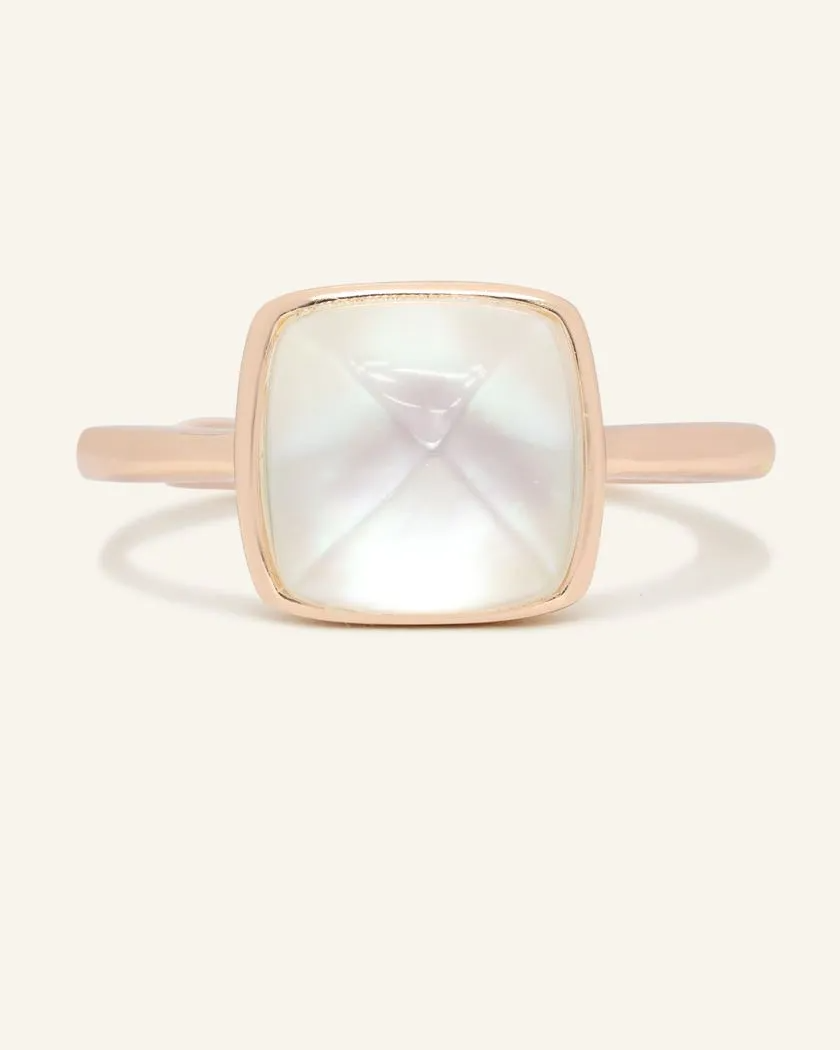 A rose gold ring featuring a large, faceted clear quartz stone cut in a sugarloaf shape, set in a simple, square bezel setting.
