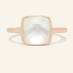 A rose gold ring featuring a large, faceted clear quartz stone cut in a sugarloaf shape, set in a simple, square bezel setting.
