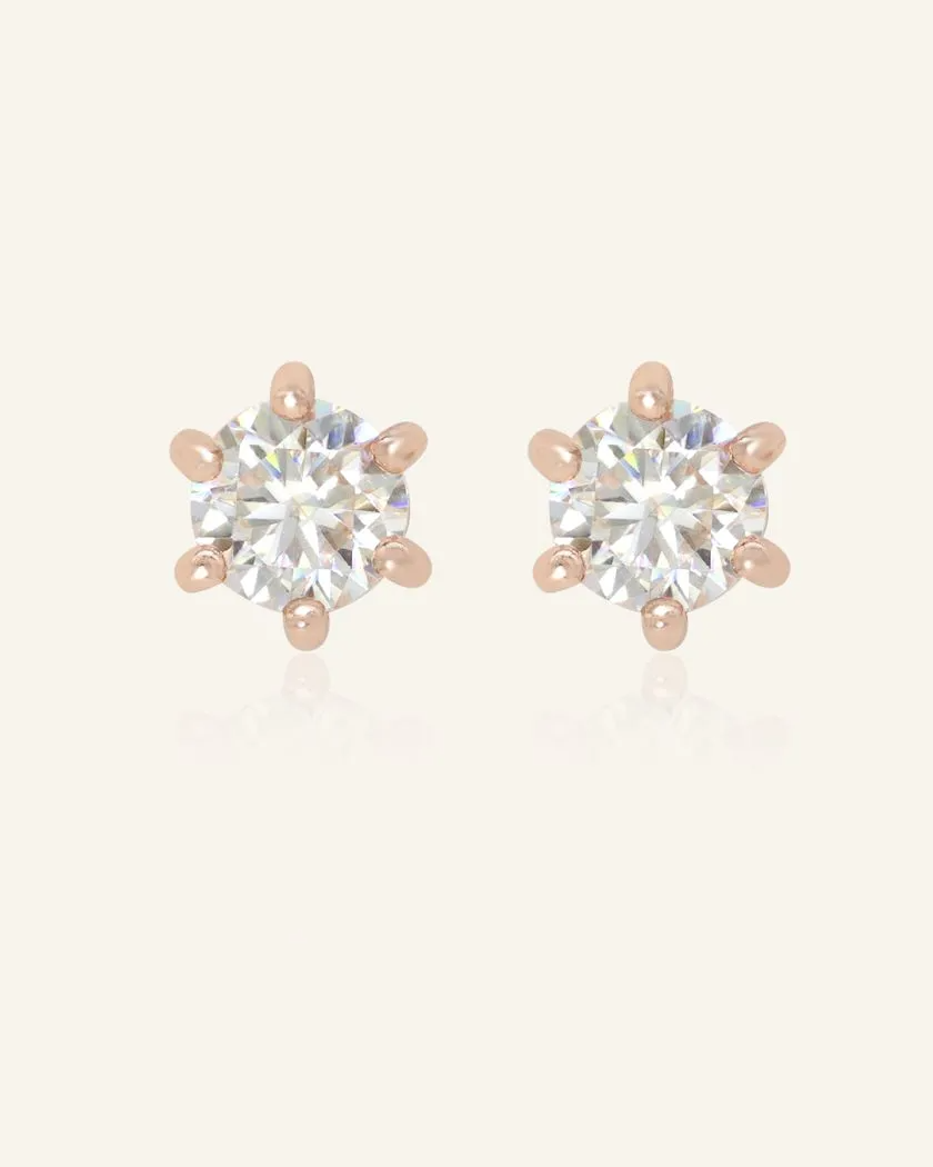A pair of dainty white moissanite stud earrings set in rose gold, featuring sparkling round-cut gemstones with a six-prong setting.	