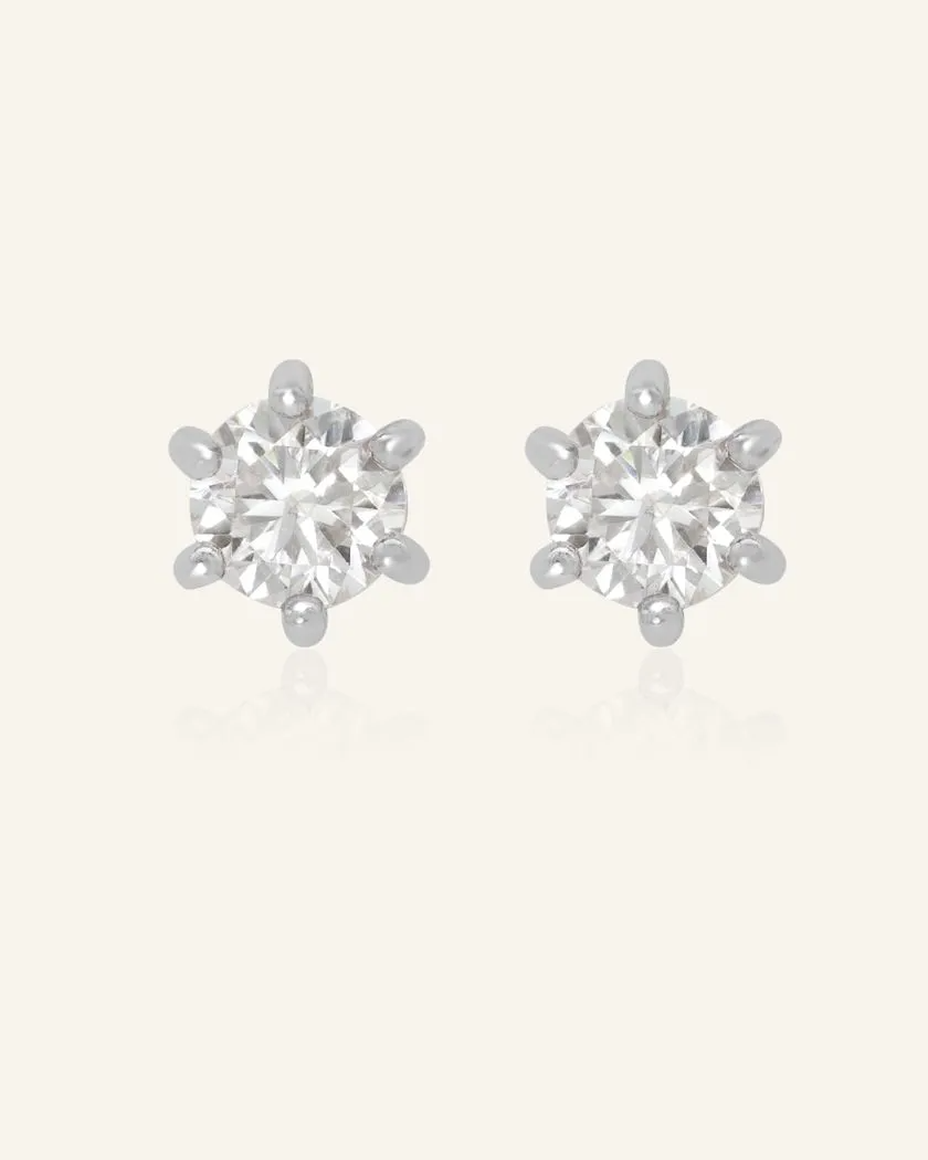 A pair of dainty white moissanite stud earrings set in silver, featuring sparkling round-cut gemstones with a six-prong setting.
