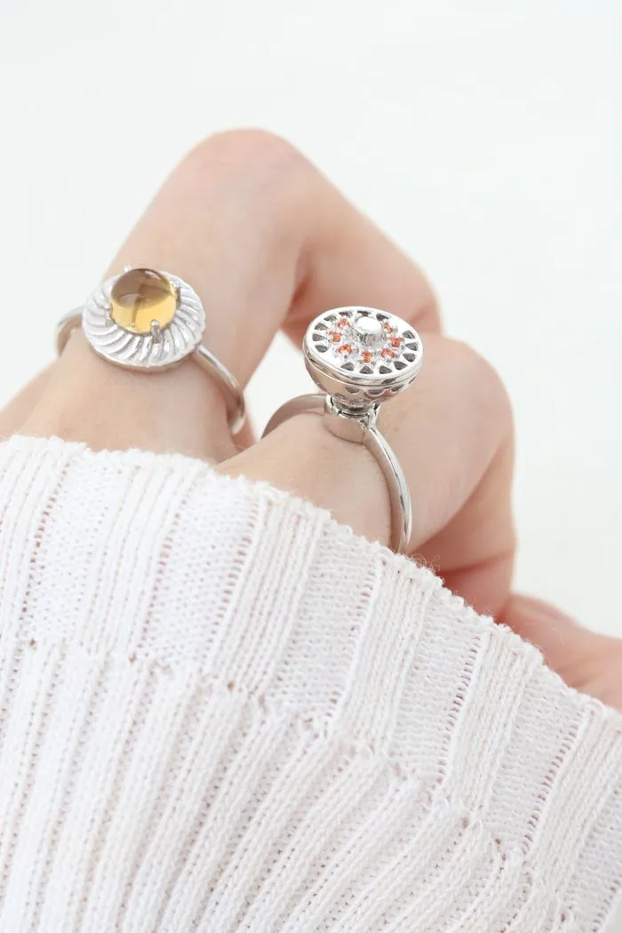 A model wearing the silver ring with a rotating circular top that opens to reveal colorful gemstones inside, resembling a spinning hotpot.