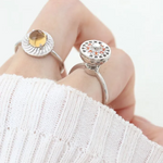 A model wearing the silver ring with a rotating circular top that opens to reveal colorful gemstones inside, resembling a spinning hotpot.