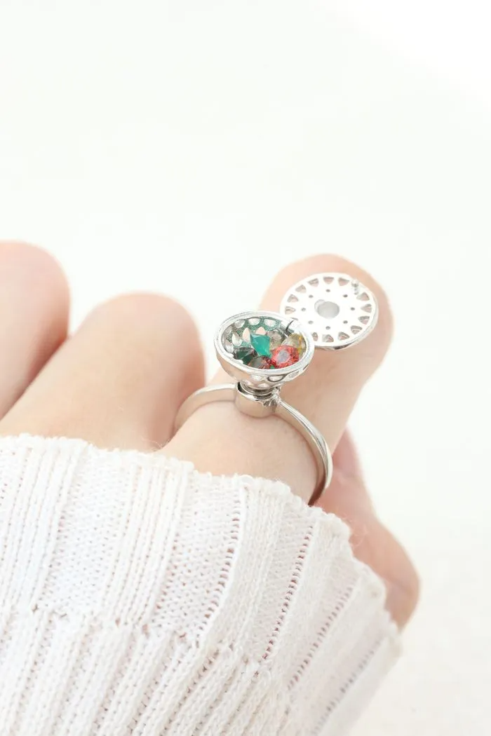 A model wearing the silver ring with a rotating circular top that opens to reveal colorful gemstones inside, resembling a spinning hotpot.