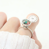 A model wearing the silver ring with a rotating circular top that opens to reveal colorful gemstones inside, resembling a spinning hotpot.