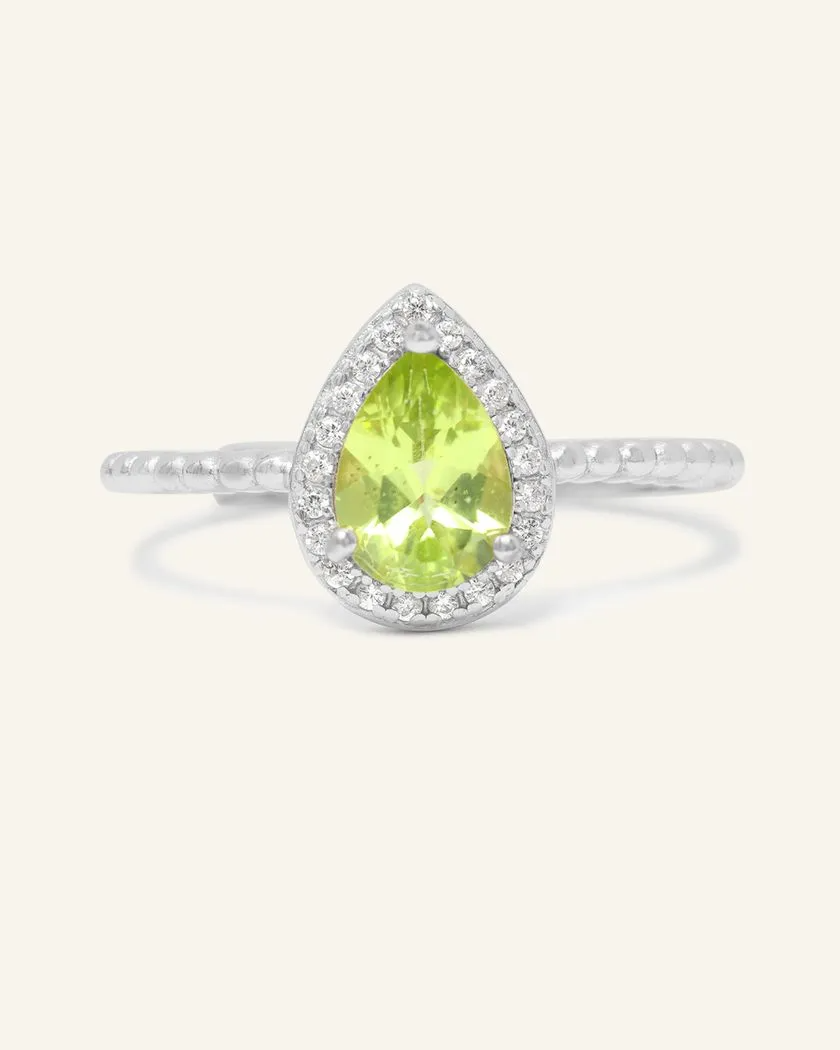 A silver ring featuring a vibrant green peridot stone cut in a teardrop shape, surrounded by a halo of small, sparkling cubic zirconias, with a textured band.
