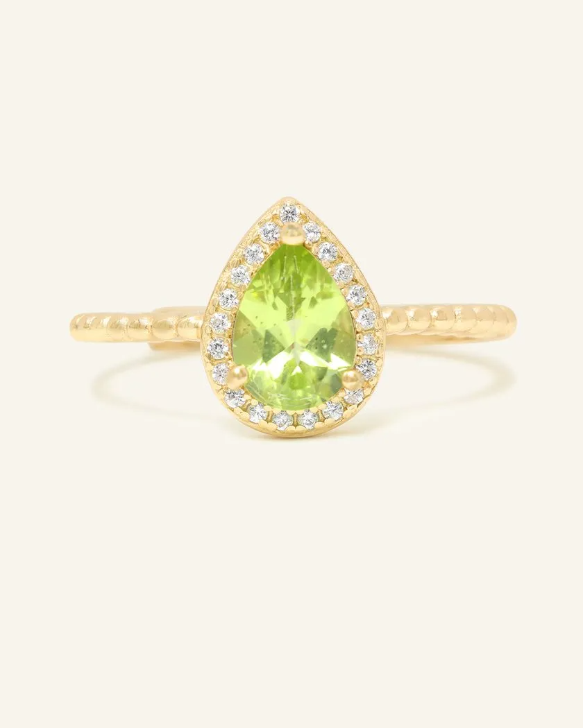 A yellow gold ring featuring a vibrant green peridot stone cut in a teardrop shape, surrounded by a halo of small, sparkling cubic zirconias, with a textured band.