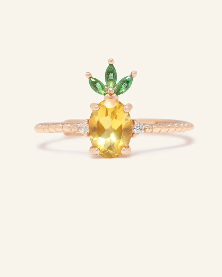 A pineapple-inspired citrine ring featuring a vibrant oval-cut yellow citrine as the centerpiece, accented with green marquise cubic zirconia as leaves and set on a delicate rose gold band.