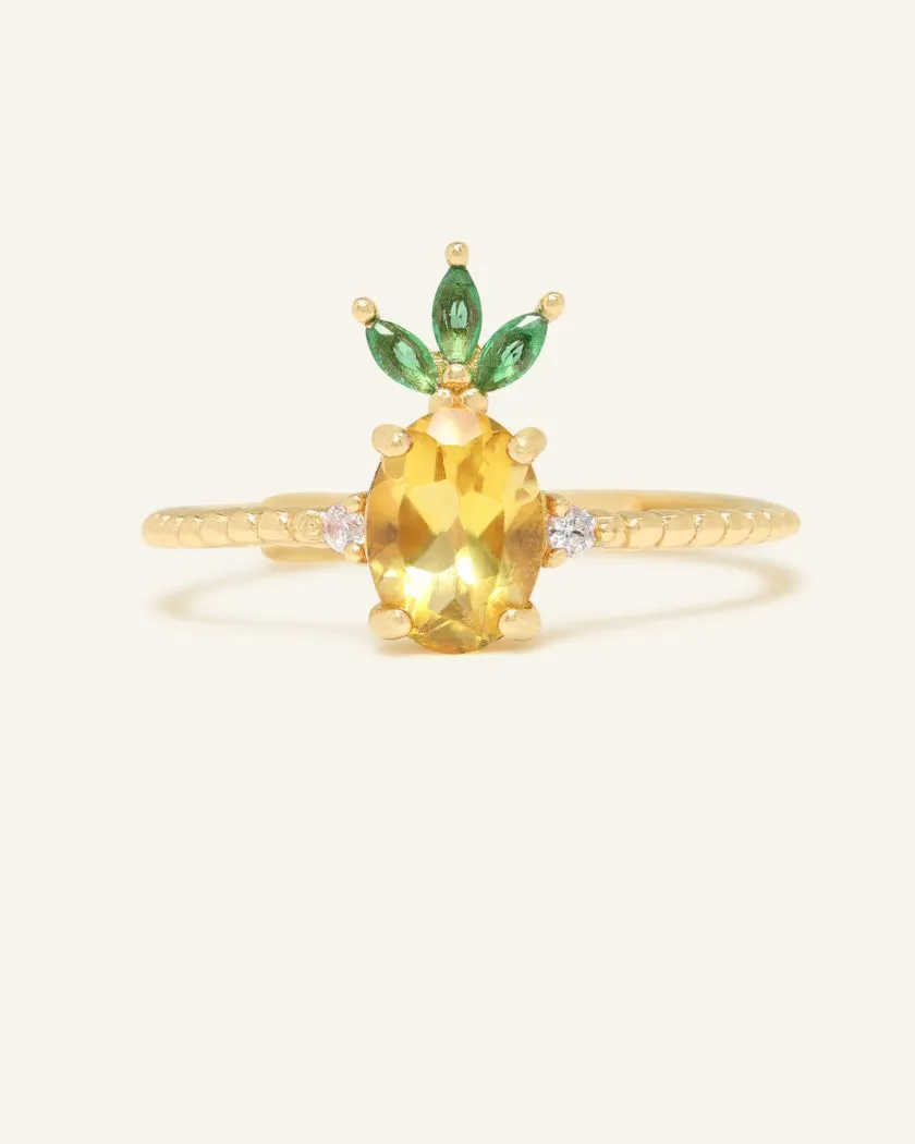 A pineapple-inspired citrine ring featuring a vibrant oval-cut yellow citrine as the centerpiece, accented with green marquise cubic zirconia as leaves and set on a delicate yellow gold band.
