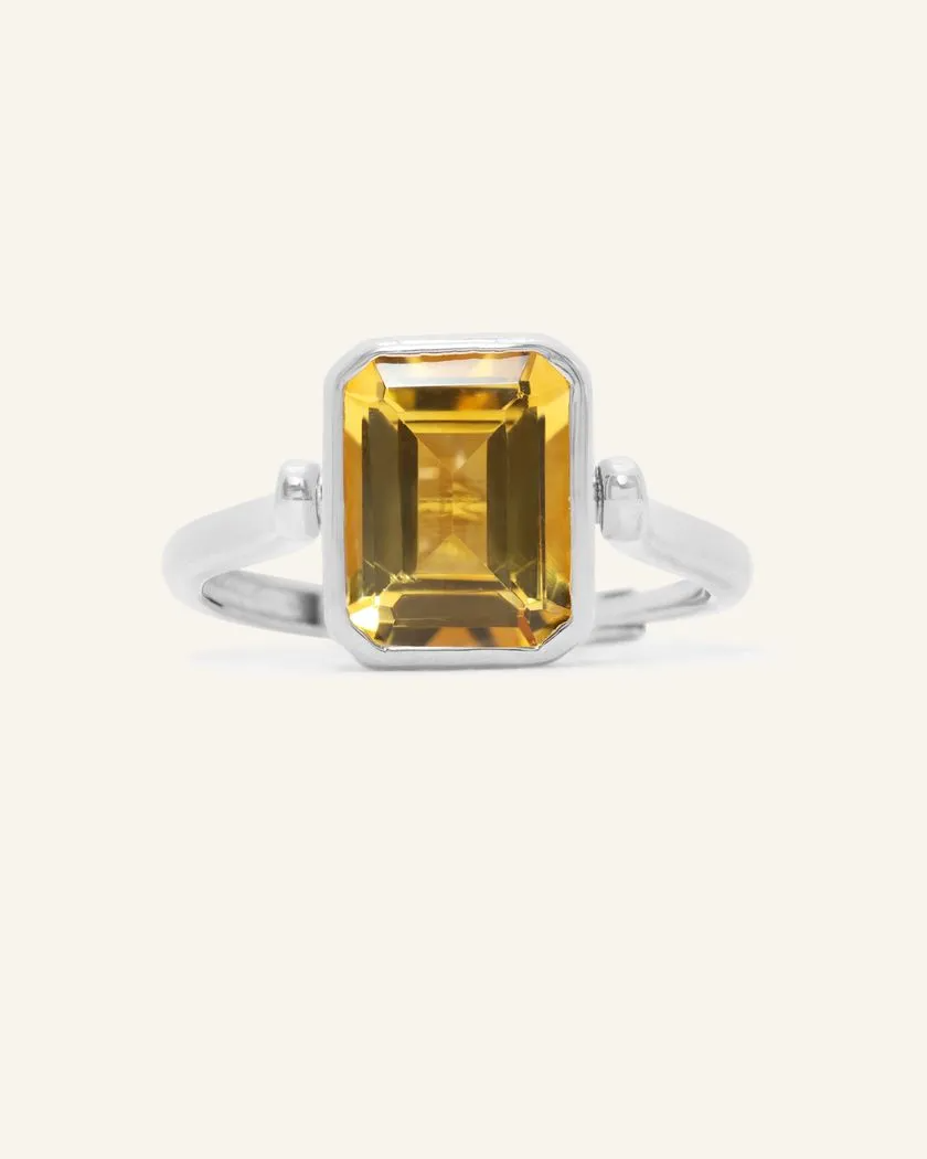 A silver ring featuring a reversible rectangular citrine gemstone adorned with intricate carvings and surrounded by cubic zirconias.