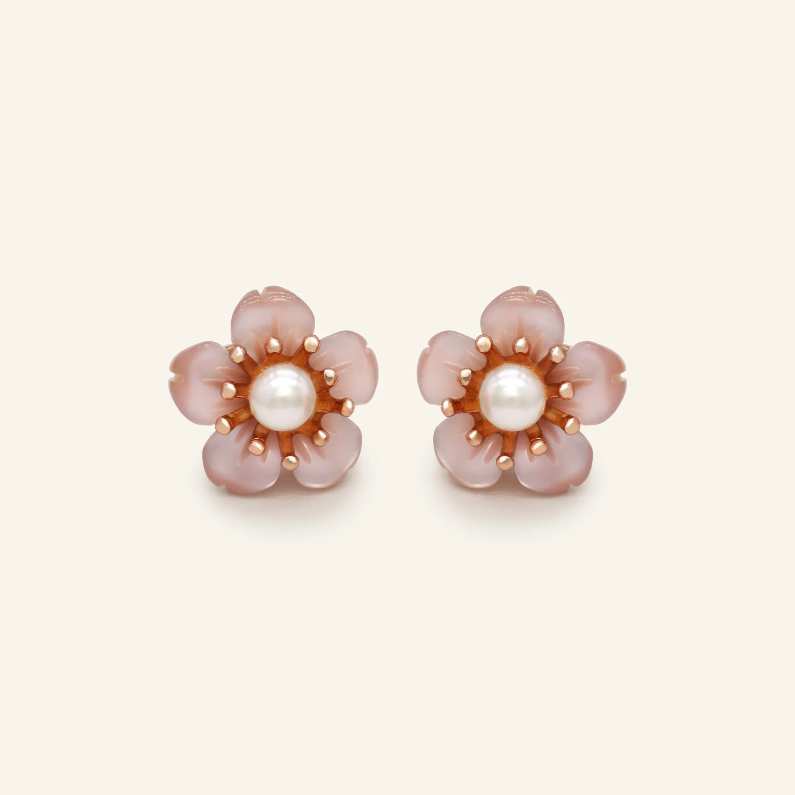 Pair of sakura stud earrings featuring a central freshwater pearl surrounded by delicately hand-carved mother-of-pearl petals in a soft pink hue, set in a rose gold-tone design.