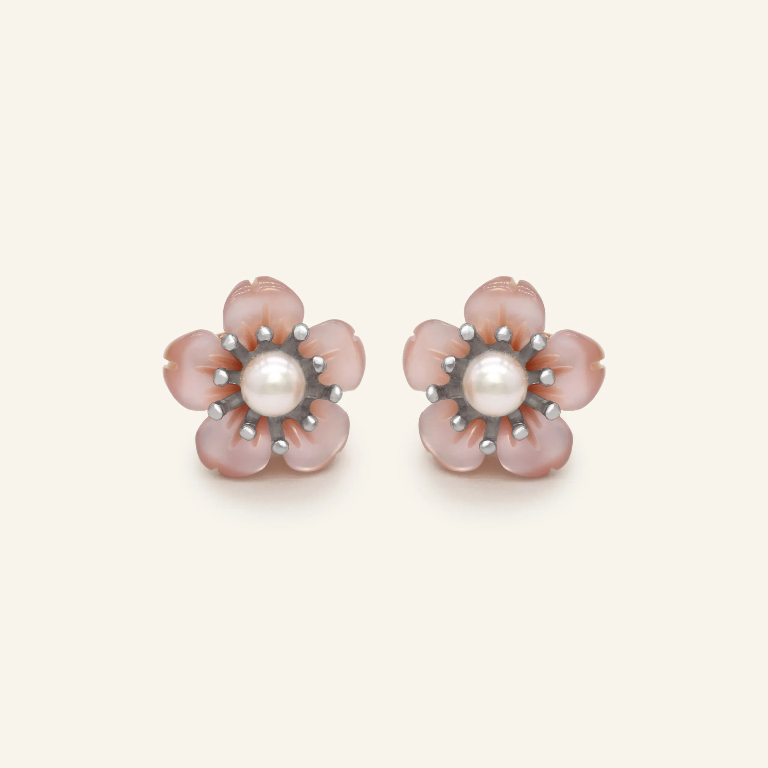 Pair of sakura stud earrings featuring a central freshwater pearl surrounded by delicately hand-carved mother-of-pearl petals in a soft pink hue, set in a silver-tone design.