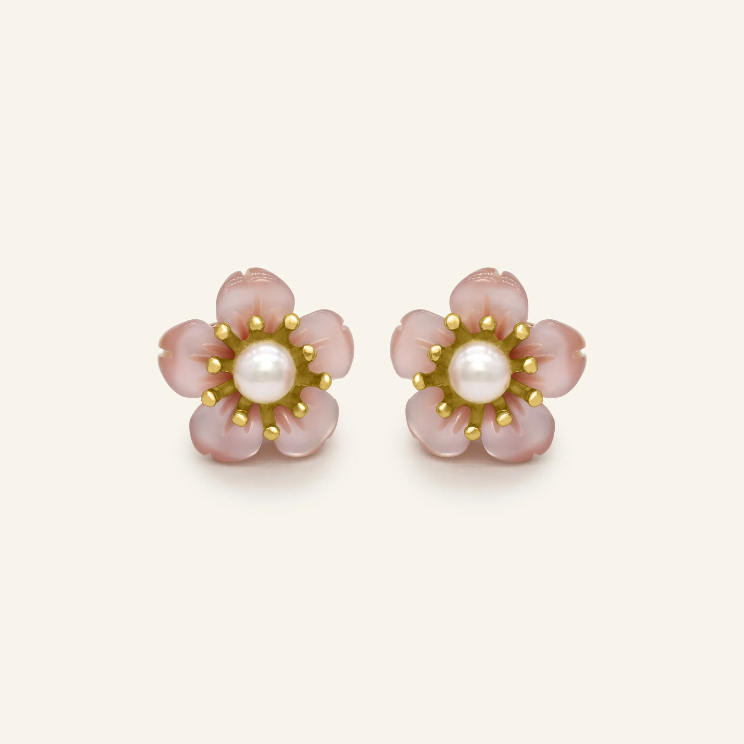 Pair of sakura stud earrings featuring a central freshwater pearl surrounded by delicately hand-carved mother-of-pearl petals in a soft pink hue, set in a yellow gold-tone design.