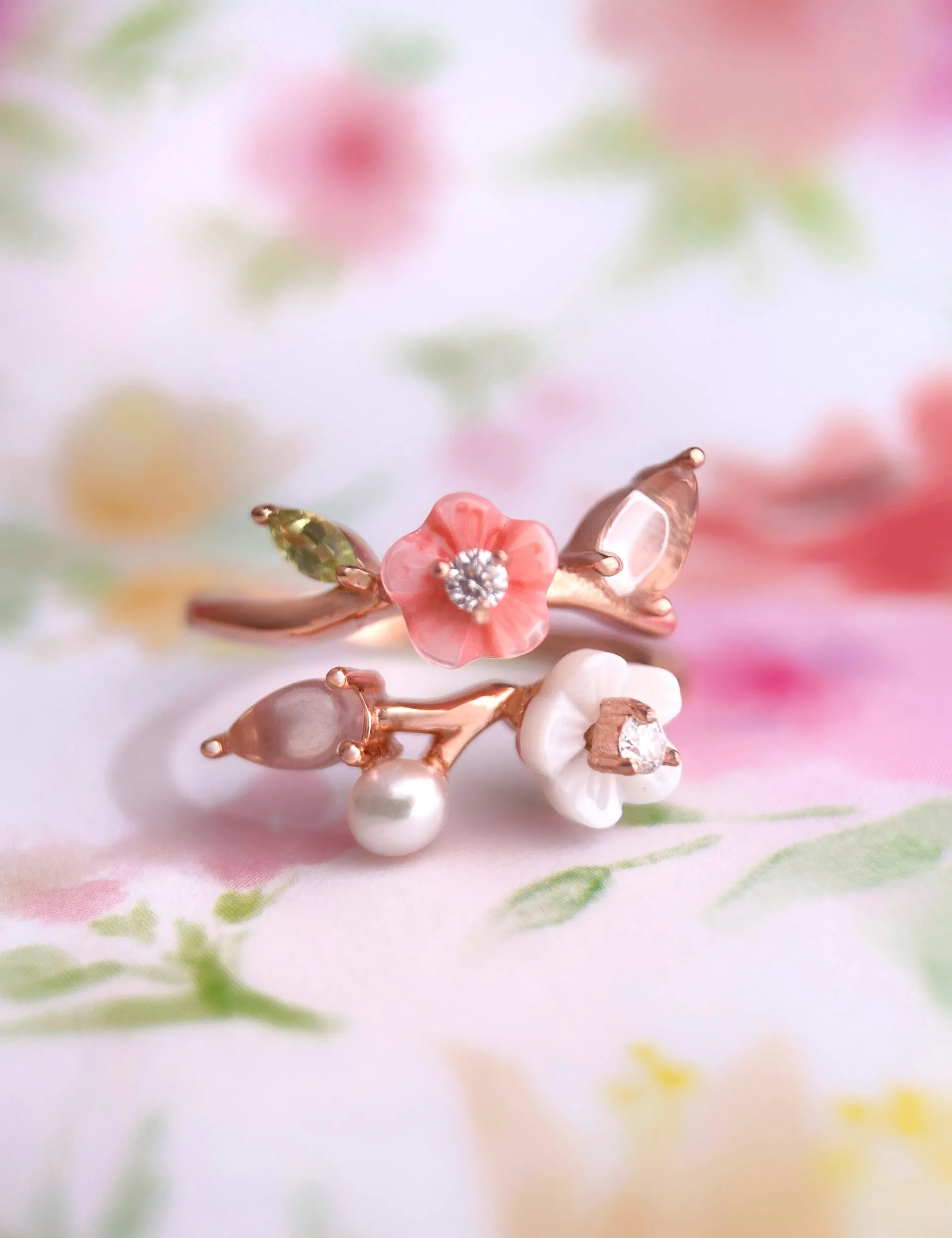 A rose gold Sakura Symphony Ring adorned with peridot, freshwater pearl, rose quartz, hand-carved shell flowers, and sparkling moissanite accents, capturing the essence of spring blossoms.